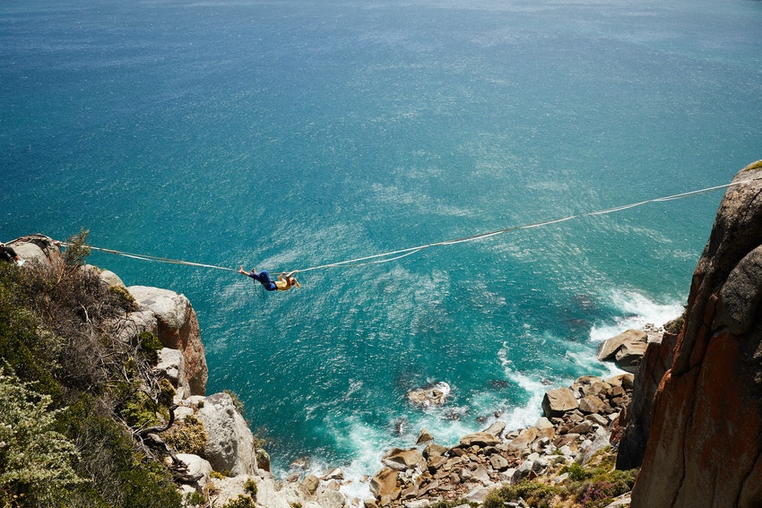 femme qui descend la tyrolienne au dessus de la mer sur une falaise