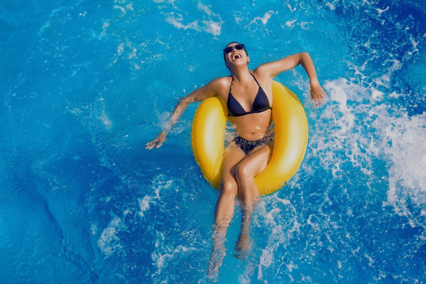 jeune femme en maillot de bain qui rigole allongee sur une bouee jaune dans une piscine