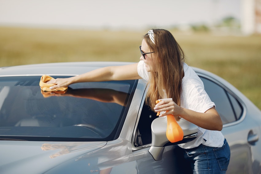 Jeune femme nettoyant une voiture en rigolant