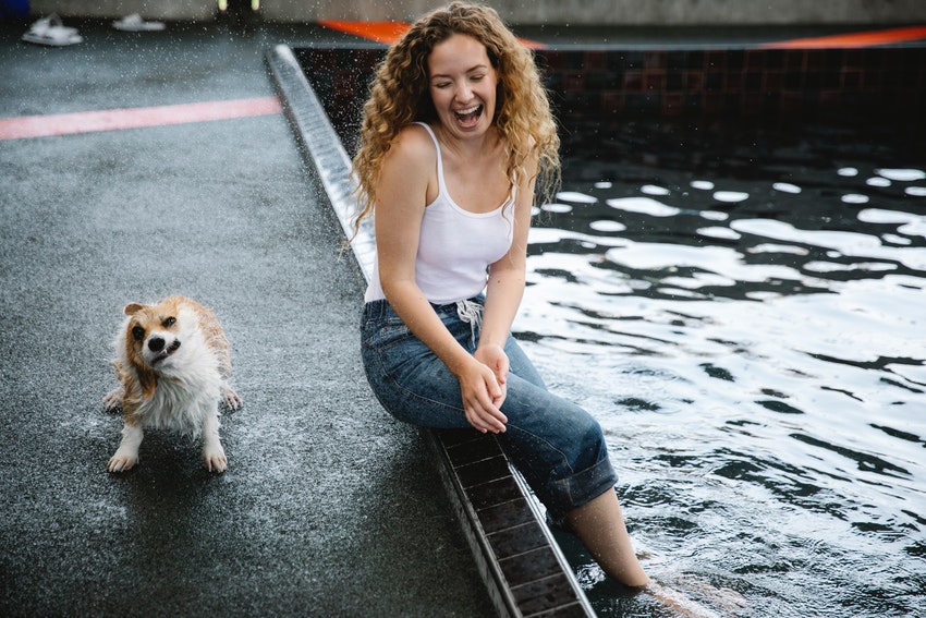 Une femme assise au bord de l'eau avec un chien qui se secoue