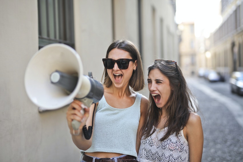 deux amies criant dans un megaphone dans la rue