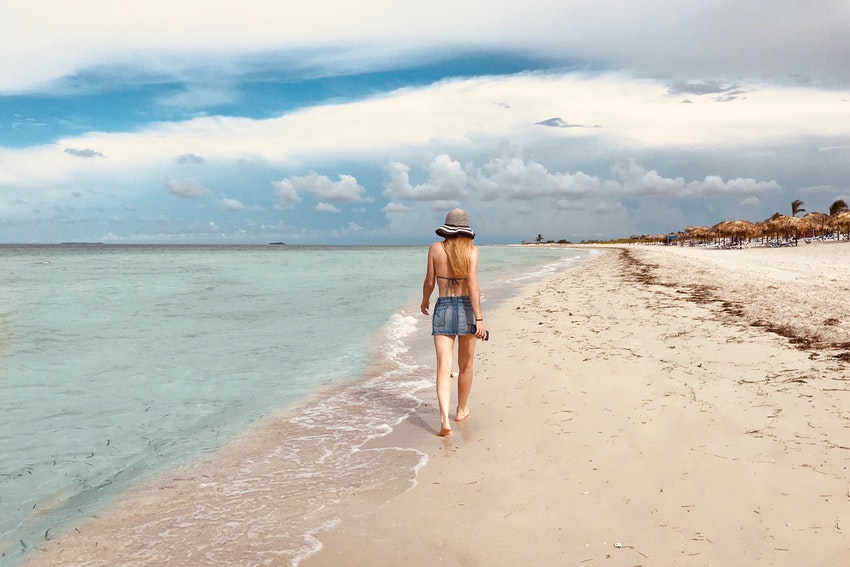 femme a la plage les pieds dans l'eau portant un chapeau