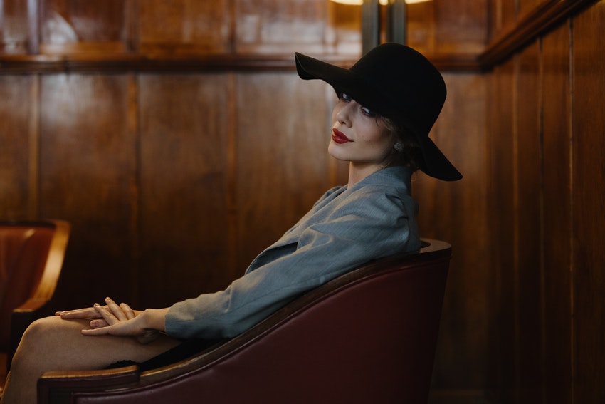 femme fatale assise sur une chaise dans un bar portant un chapeau noir