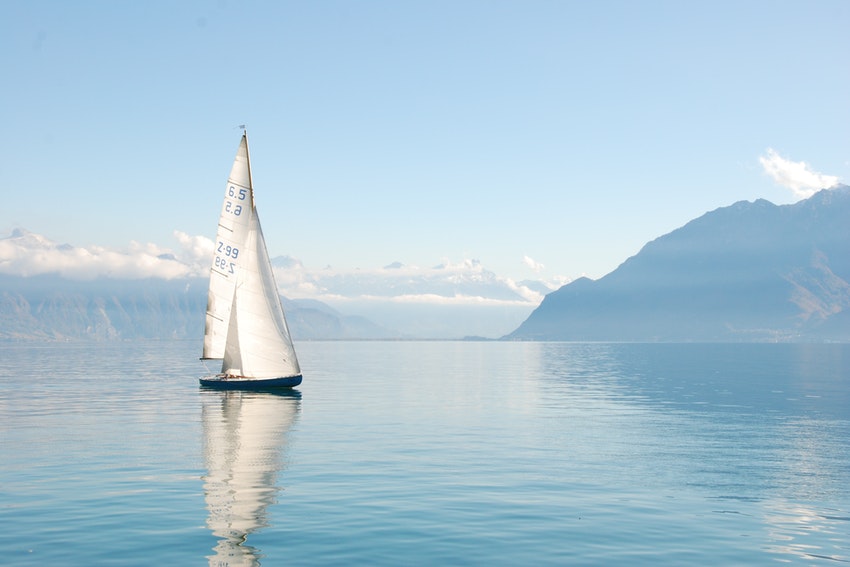 grand voilier refletant sur l'eau avec un paysage de montagne a l horizon