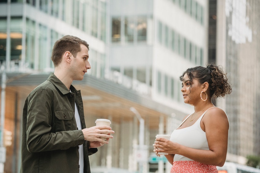 un homme et une femme dans la rue discutant avec un café à la main