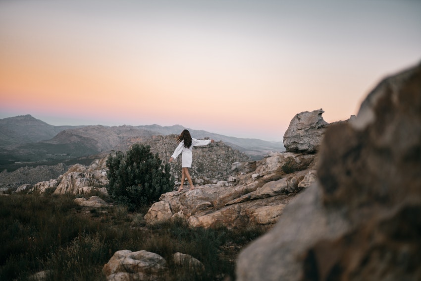 femme en robe blanche qui marche sur des rochers au coucher du soleil