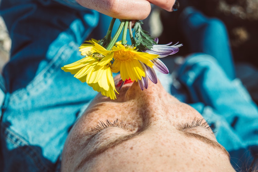 jeune femme qui sent des fleurs jaunes et violettes