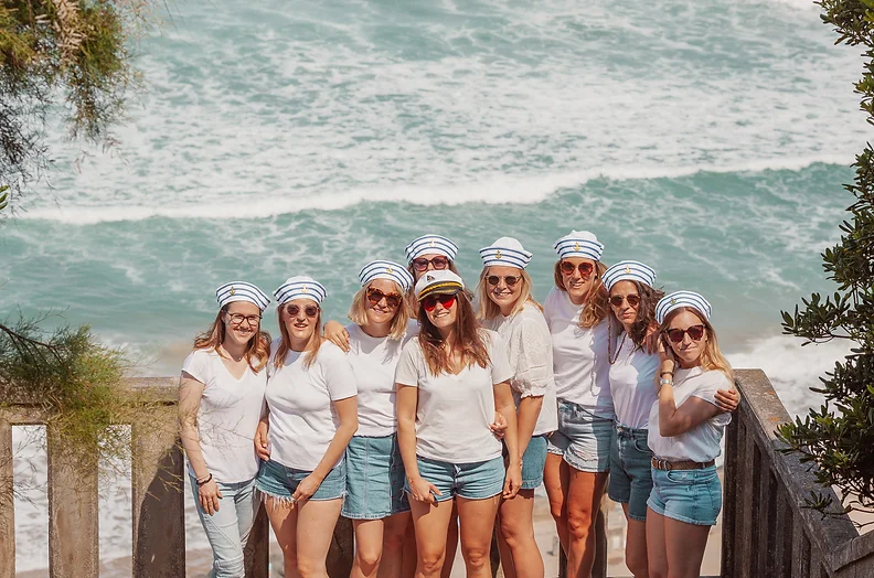 Groupe de femmes célébrant un EVJF à Biarritz, posant en tenues marines avec des casquettes de marin, devant l’océan Atlantique.