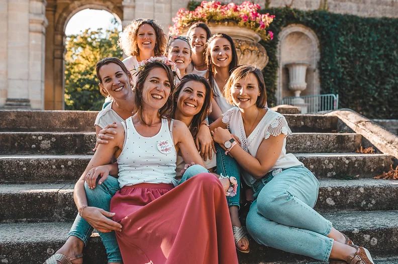 Groupe de femmes célébrant un EVJF à Bordeaux, assises sur des marches avec des fleurs et des monuments historiques en arrière-plan.