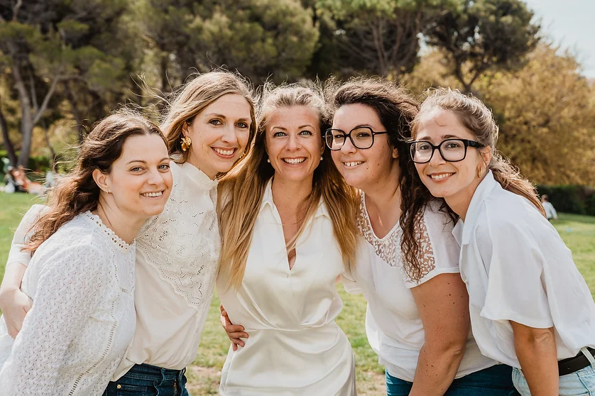 Groupe de femmes souriantes célébrant un EVJF à Caen, posant dans un parc verdoyant sous un ciel ensoleillé.