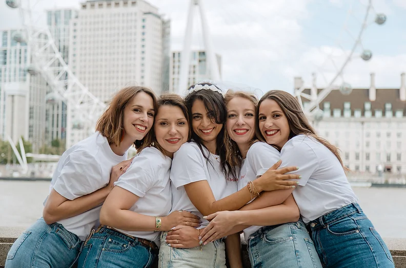 Groupe de femmes célébrant un EVJF à Londres avec le London Eye en arrière-plan, partageant des moments de complicité et de joie.