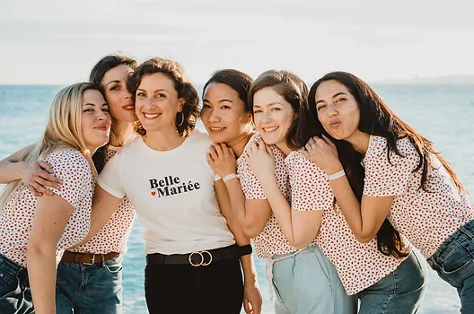 Groupe de femmes célébrant un EVJF à Nice, posant joyeusement en bord de mer avec des tenues coordonnées et un t-shirt 'Belle Mariée'