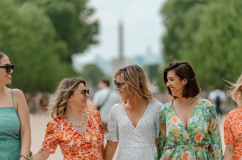 Trois femmes souriantes célébrant un EVJF à Paris, marchant dans un parc avec la Tour Eiffel visible en arrière-plan.