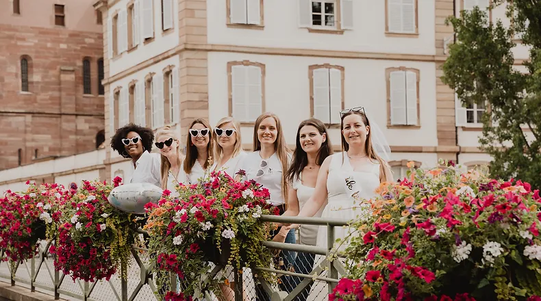 Groupe de femmes célébrant un EVJF à Strasbourg, posant sur un pont fleuri devant des bâtiments historiques.