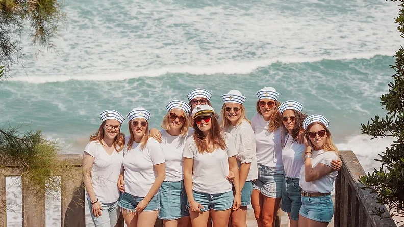 Groupe de femmes célébrant un EVJF à Biarritz, posant en tenues marines avec des casquettes de marin, devant l’océan Atlantique.