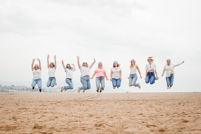 Groupe de filles EVJF sautant en l’air sur la plage de La Baule, avec lunettes en forme de cœur et couronnes de fleurs