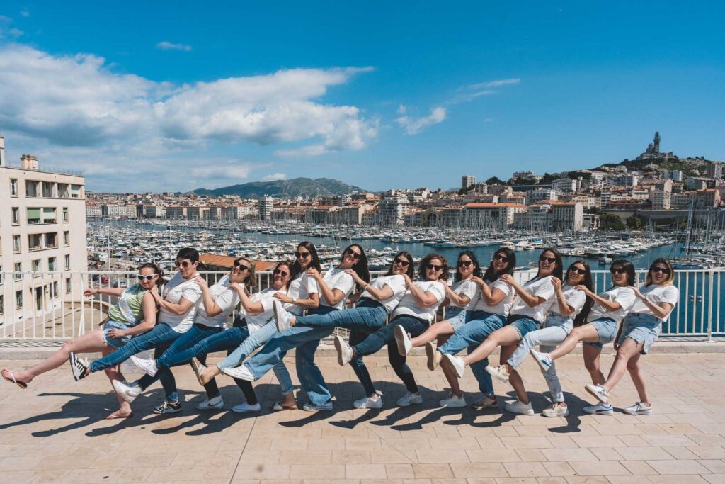 Un groupe de femmes en tenue coordonnée posant dans une ambiance festive face au Vieux-Port de Marseille, lors du tournage d’un clip vidéo EVJF.