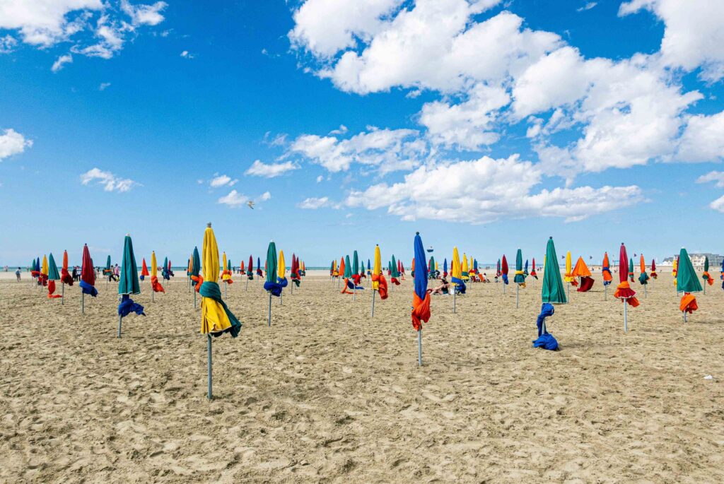 Un pique-nique raffiné est installé sur le sable, avec paniers en osier, salades en bocaux, gourmandises et boissons naturelles, face à la mer de Deauville au coucher du soleil.