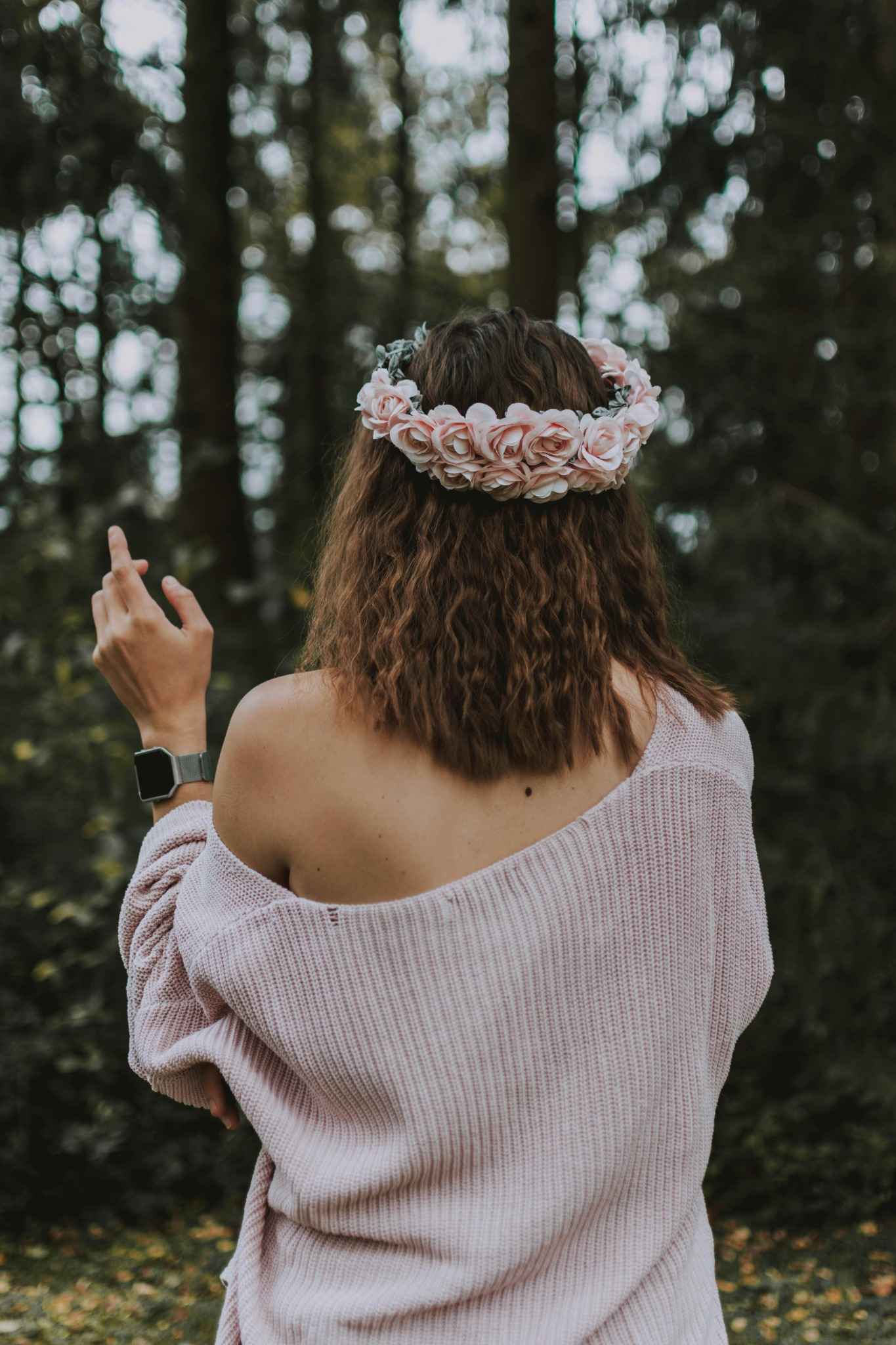 Femme de dos portant une couronne de fleurs roses en pleine nature, vêtue d’un pull rose tombant sur l’épaule, lors d’un atelier floral EVJF à Deauville.