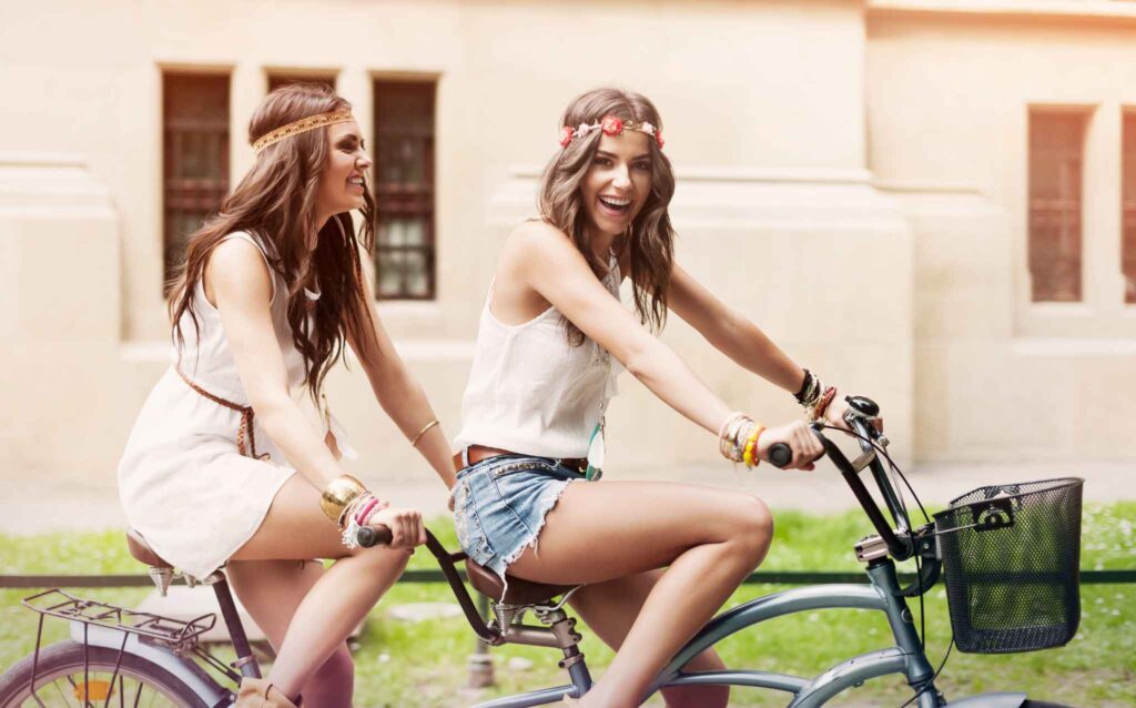 Deux jeunes femmes souriantes en robe d’été lors d’une balade en vélo à Deauville pendant un EVJF