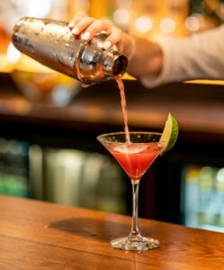 Une participante verse un cocktail coloré dans un verre à martini lors d’un atelier de mixologie EVJF à Annecy.