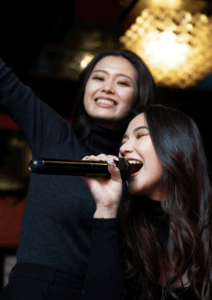 Deux amies chantent ensemble au karaoké pendant un EVJF, micro en main, souriantes et pleines d’énergie.
