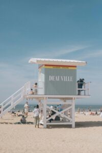 Groupe de femmes célébrant un EVJF autour d’un dîner festif sur la plage de Deauville, pieds nus dans le sable, face à la mer au coucher du soleil.