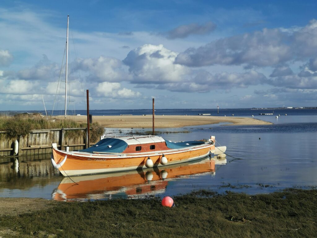 Pinasse traditionnelle naviguant sur les eaux calmes du Bassin d’Arcachon sous un ciel bleu, avec en fond la côte landaise.