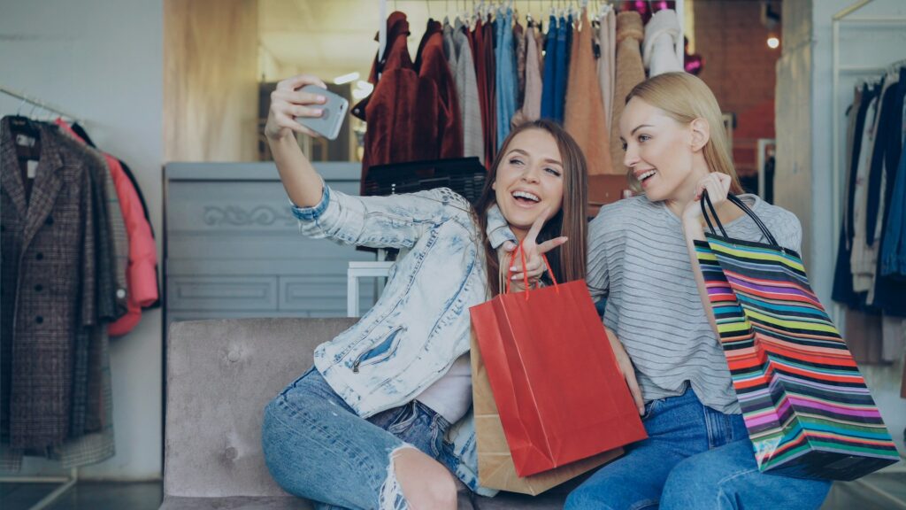 Deux amies souriantes prennent un selfie avec des sacs de shopping à San Sebastian