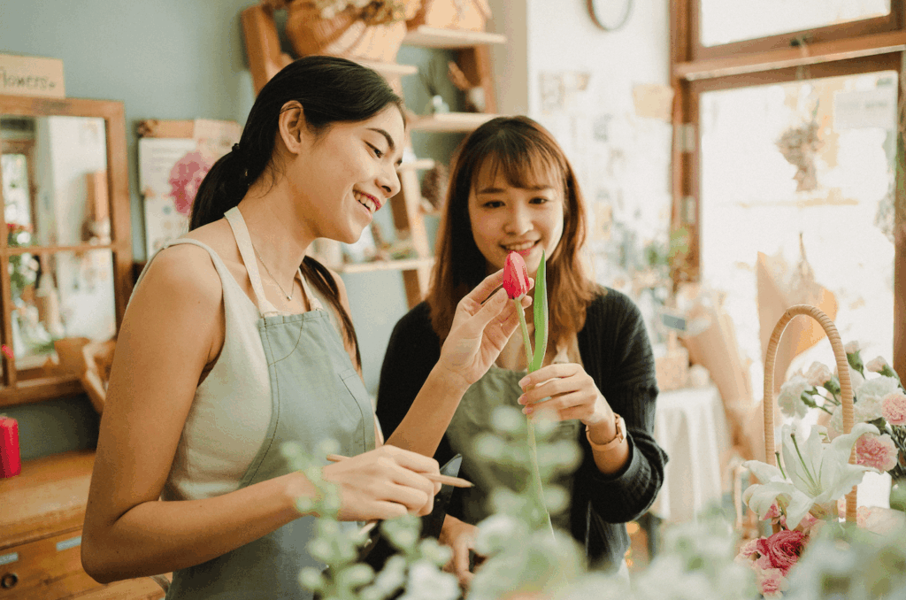 Deux femmes souriantes réalisant une couronne de fleurs lors d’un atelier créatif pour un enterrement de vie de jeune fille (EVJF)