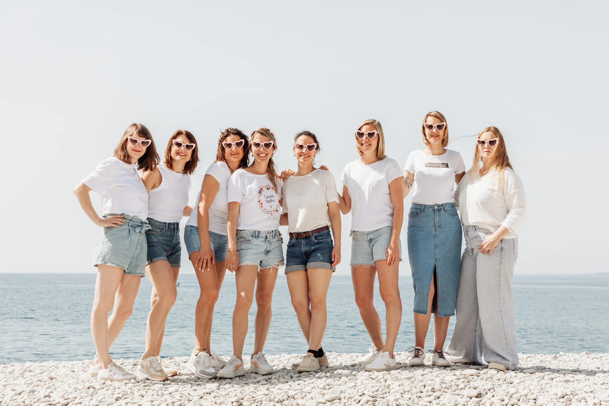 Groupe EVJF à Nice célébrant la future mariée sur la plage avec tenues assorties rose et blanc face à la mer Méditerranée