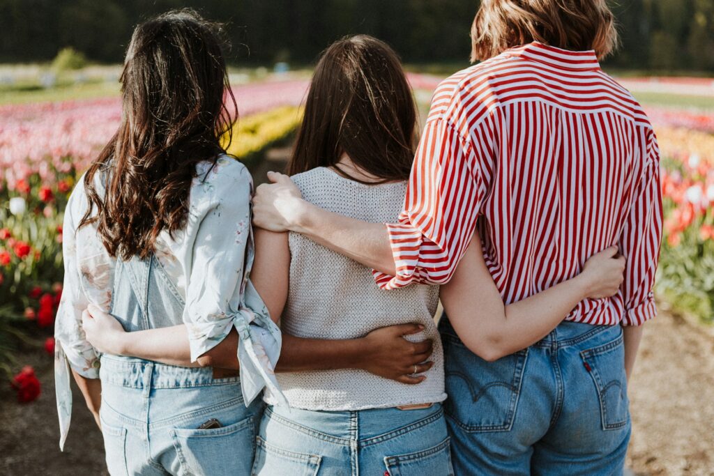 Trois femmes de dos, se tenant par les épaules dans un jardin fleuri lors d’un EVJF.