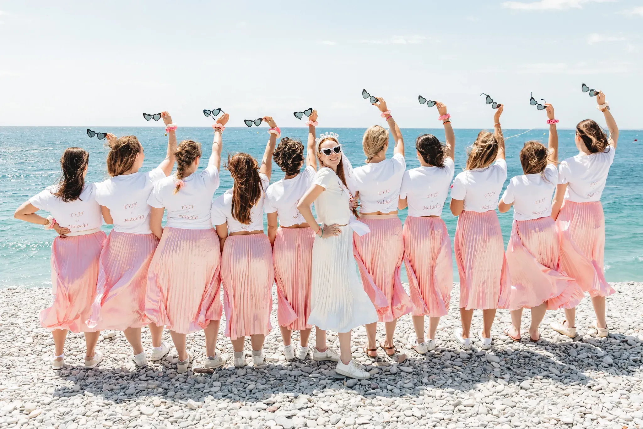 Groupe de filles en EVJF en France posant sur la plage avec tenues coordonnées et lunettes cœur, ambiance festive et complicité