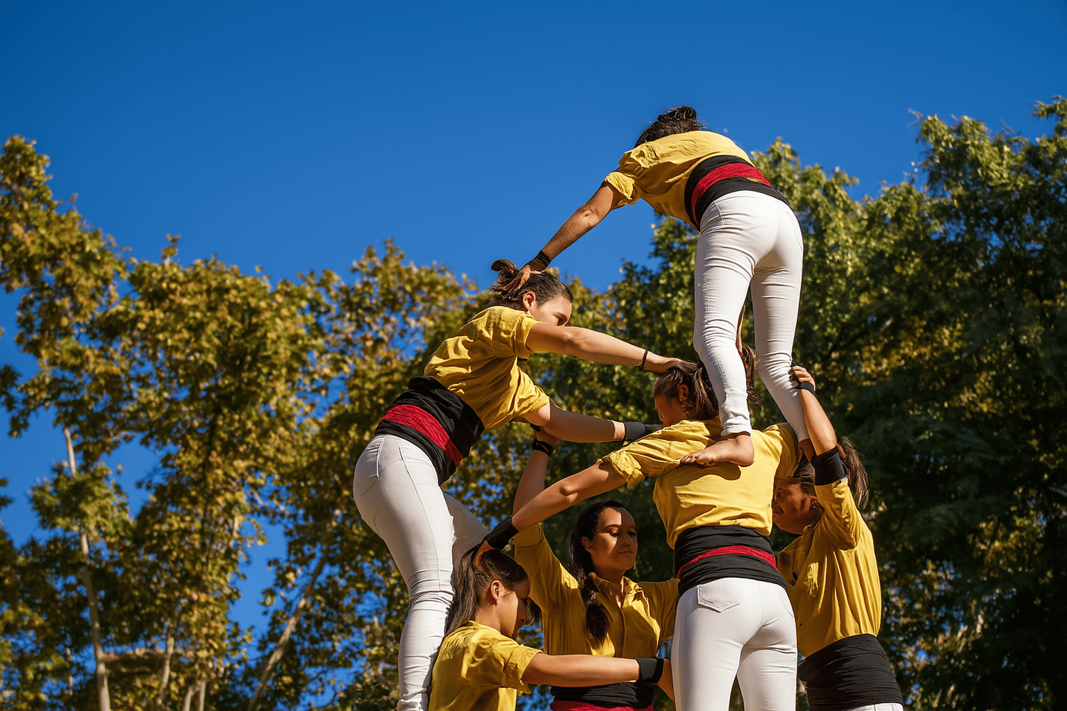 Jeunes femmes en tenue coordonnée réalisant une pyramide humaine pour un EVJF à Biarritz, sous un ciel bleu et des arbres dorés.