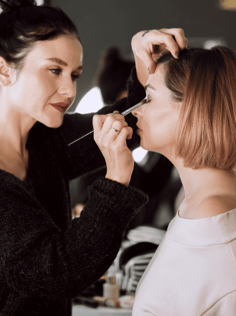 Future mariée en train de se faire maquiller lors d’un EVJF à Strasbourg, pendant qu’un groupe de filles reçoit des conseils beauté d’une professionnelle.