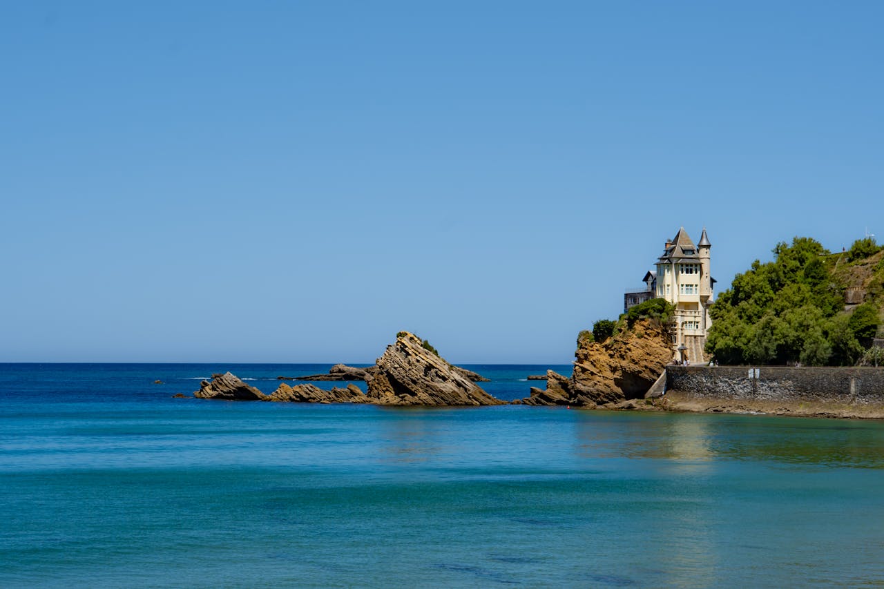 alt="Vue panoramique sur la villa Belza et les rochers de Biarritz depuis un bateau de croisière EVJF, avec mer turquoise et ciel dégagé, typique d'une sortie privatisée sur la côte basque."