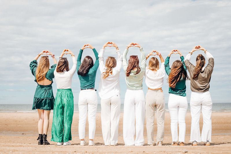 Groupe de jeunes femmes debout sur la plage à La Rochelle, de dos, formant un cœur avec leurs mains pendant un shooting photo EVJF.