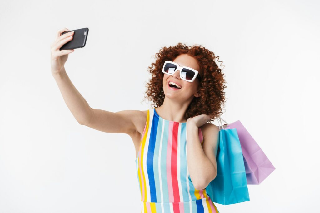 Jeune femme rieuse en train de faire un selfie avec des sacs shopping colorés