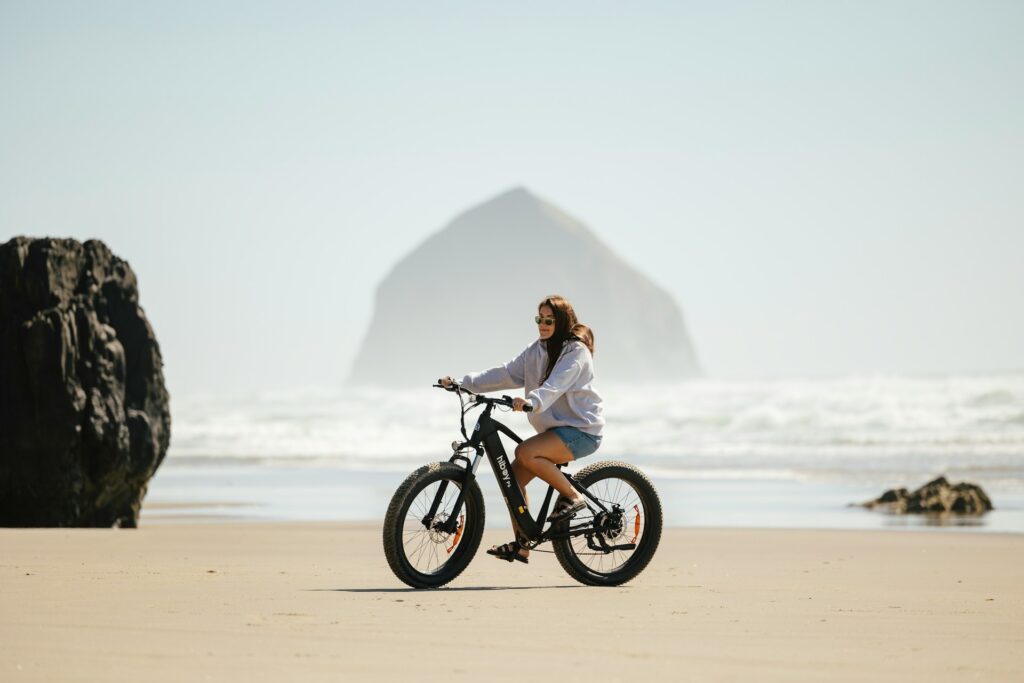Femme souriante en balade à vélo électrique sur le sable en bord de mer, EVJF à Biarritz