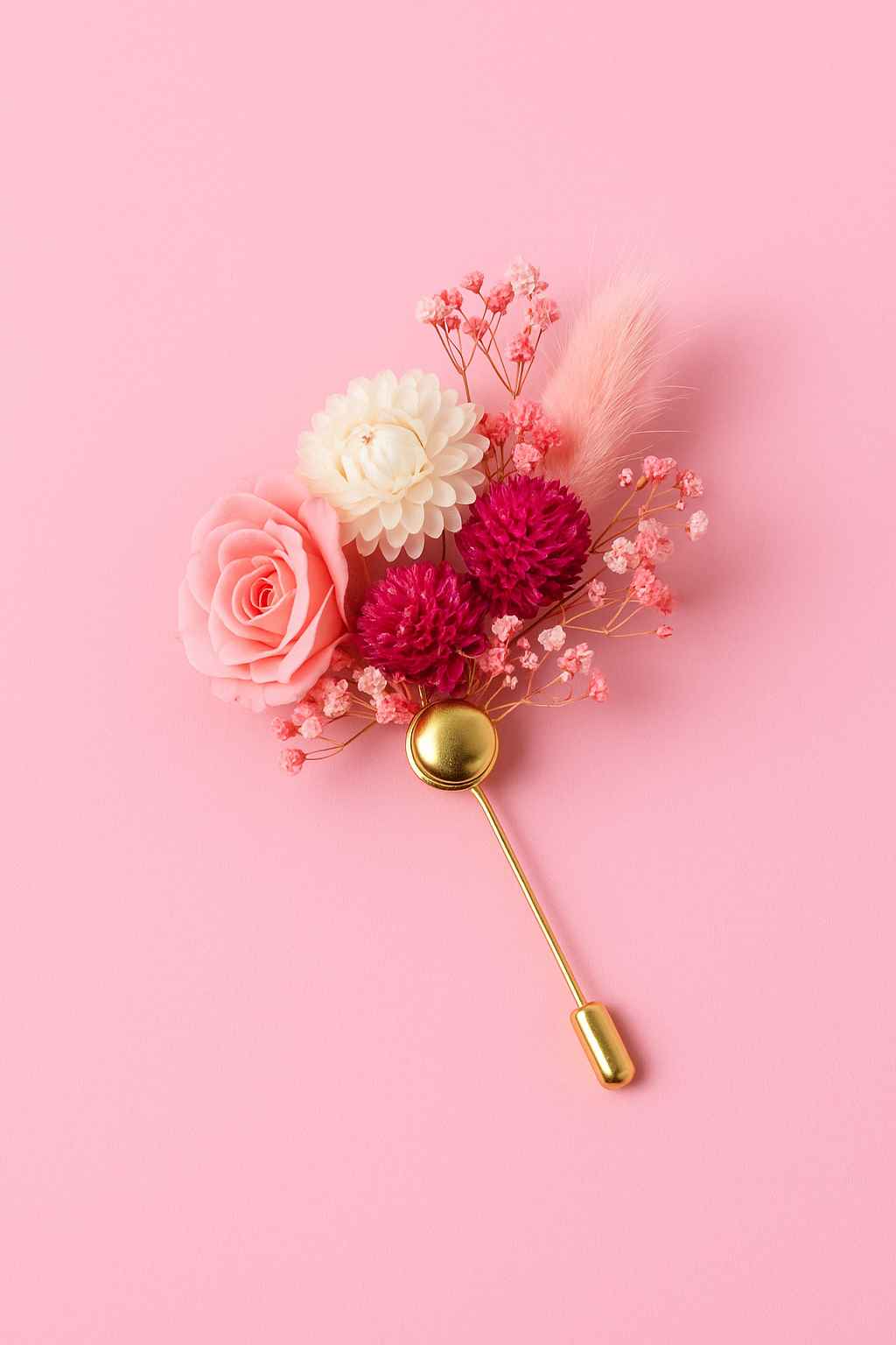 Broche florale élégante composée de fleurs séchées roses, blanches et fuchsia, montée sur une épingle dorée, posée sur un fond rose pastel – parfaite pour un atelier EVJF à Deauville.