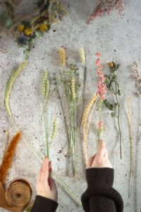 Mains sélectionnant des fleurs séchées et herbes pour un atelier couronne de fleurs à Annecy pendant un EVJF.