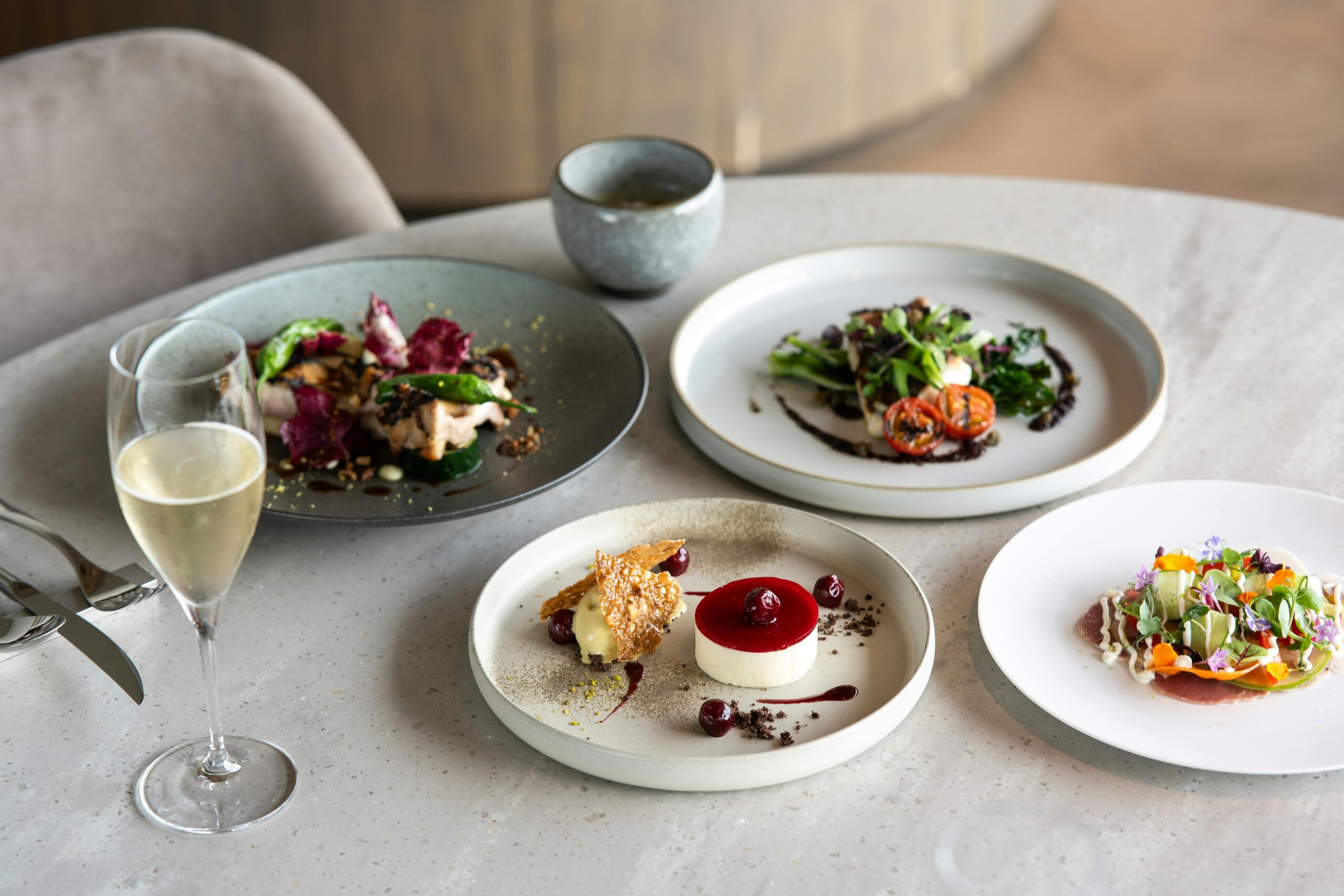 Table élégante dressée avec des assiettes gastronomiques colorées et raffinées, accompagnées d’un verre de champagne dans un restaurant chic.