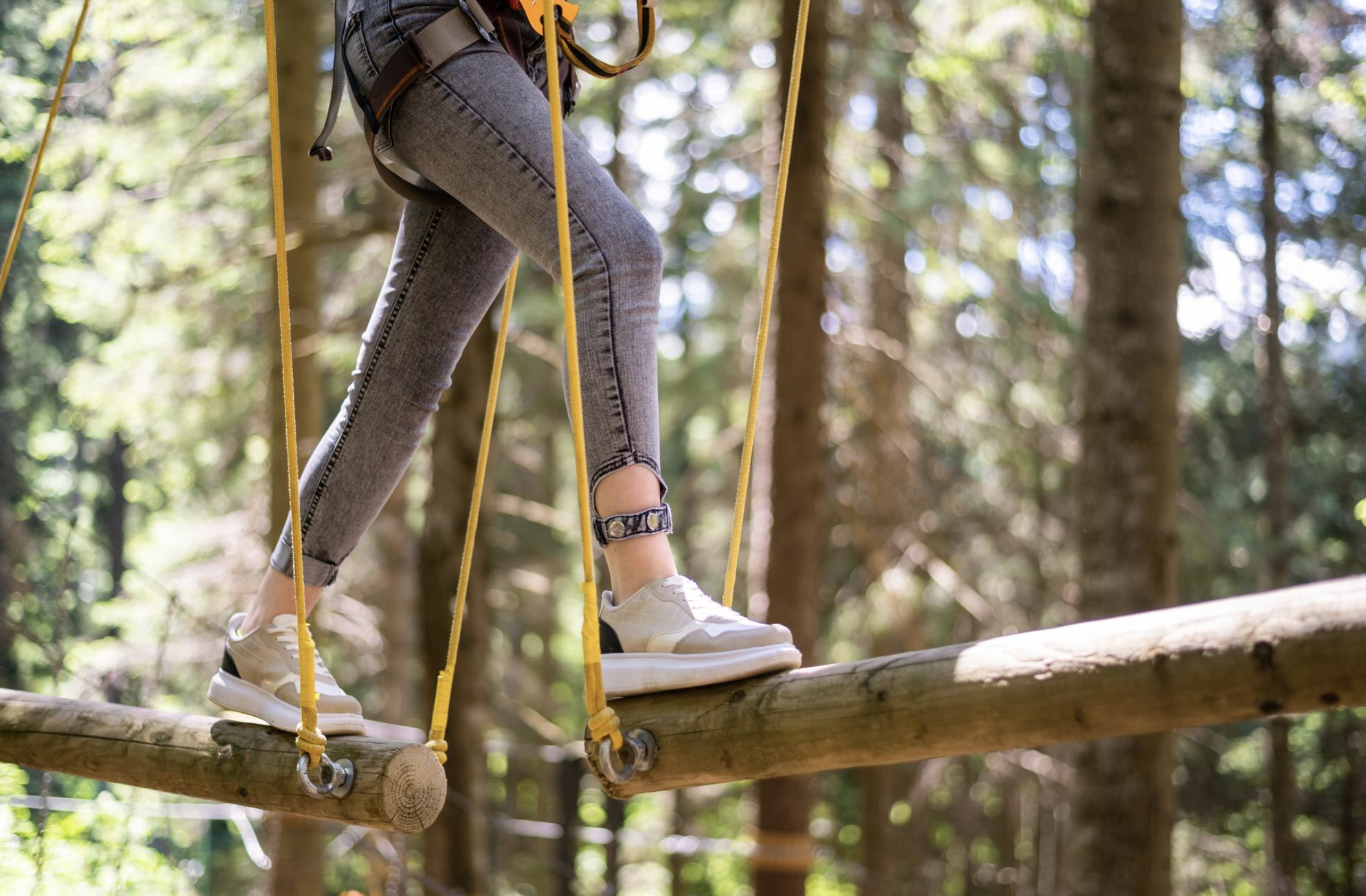Jeune femme équipée d’un baudrier, progressant seule sur un parcours d’accrobranche entre les arbres dans une forêt près d’Arcachon