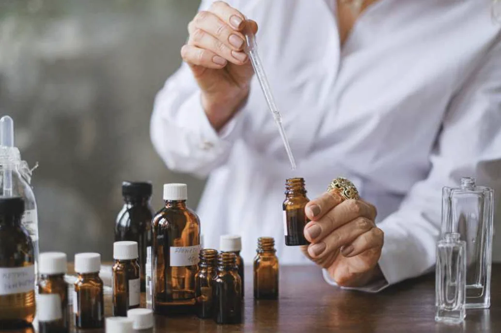 Personne preparant un melange avec une pipette et des flacons d'huiles essentielles lors d'un atelier cosmetique a Bordeaux.