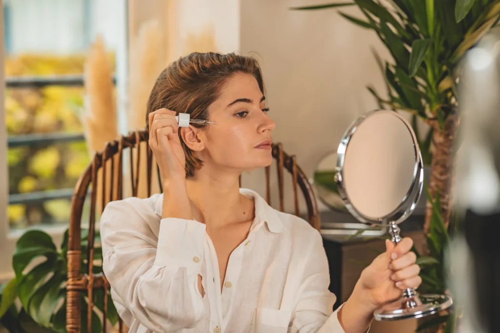 Femme appliquant un soin visage avec une pipette devant un miroir, assise dans un intérieur lumineux et naturel