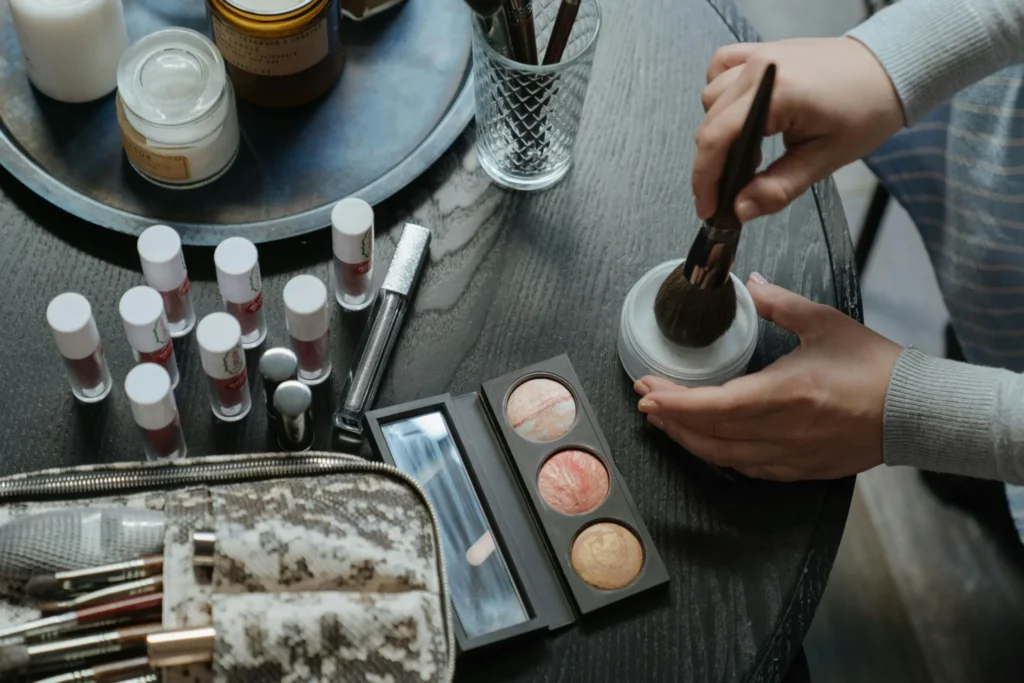 Mains utilisant un pinceau de maquillage lors d’un EVJF à Reims avec produits de beauté sur la table