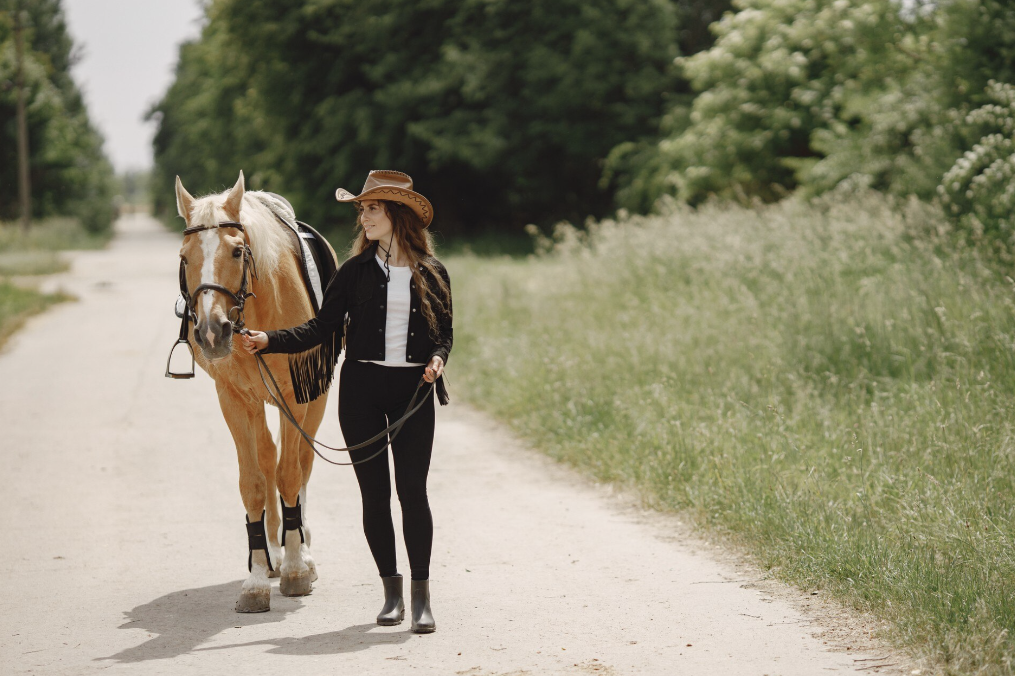 Jeune femme marchant en tenant un cheval par la bride, sur un sentier sableux bordé de pins près d’Arcachon, dans une ambiance paisible.