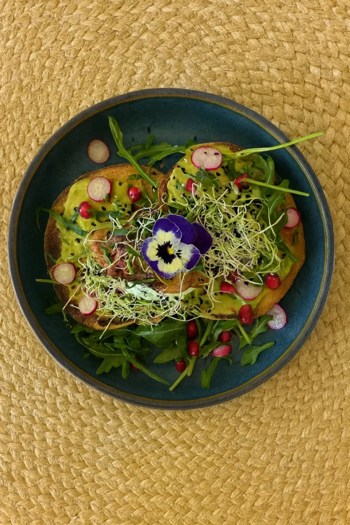Assiette gourmande avec tartines à l’avocat, radis, grenade, pousses et fleur comestible