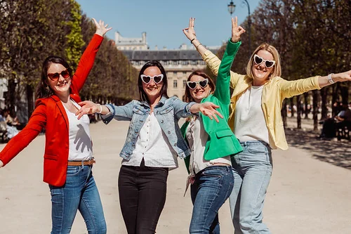 Quatre amies souriantes en vestes colorées posant bras levés lors d’un EVJF à Paris