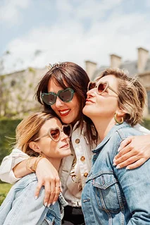Trois amies portant des lunettes en forme de cœur s’enlacent en souriant lors d’un EVJF à Paris